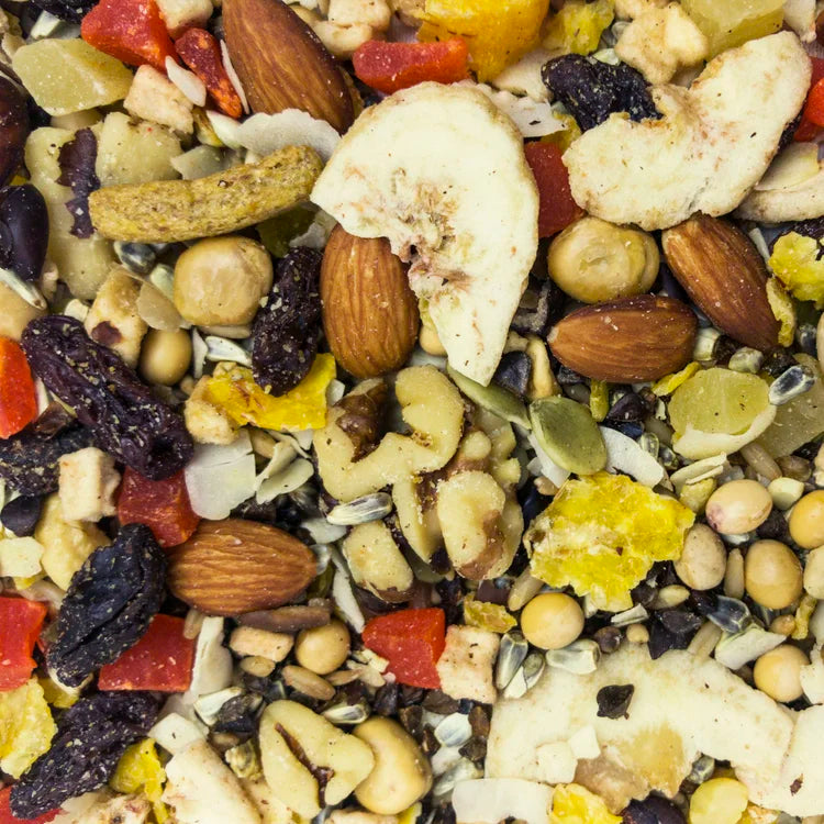 A close-up, top-down view of a mixed nut and seed snack blend, featuring almonds, cashews, pumpkin seeds, flax seeds, dried fruit pieces, and dried banana slices.