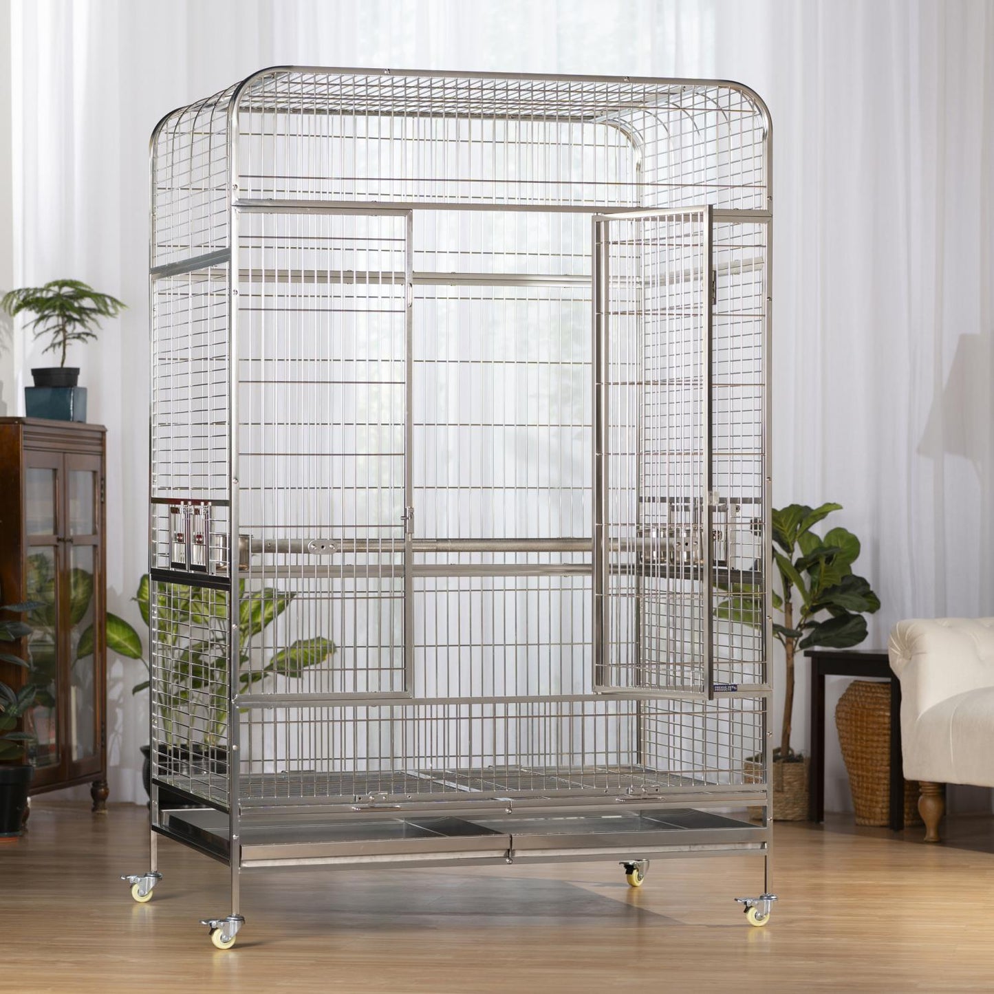 Large bird cage on wheels in a room with plants and furniture